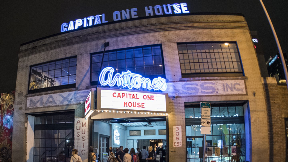 Front of a brick warehouse, blue neon sign says Antone’s. Marquee says Capital One House in red. People are lined up outside