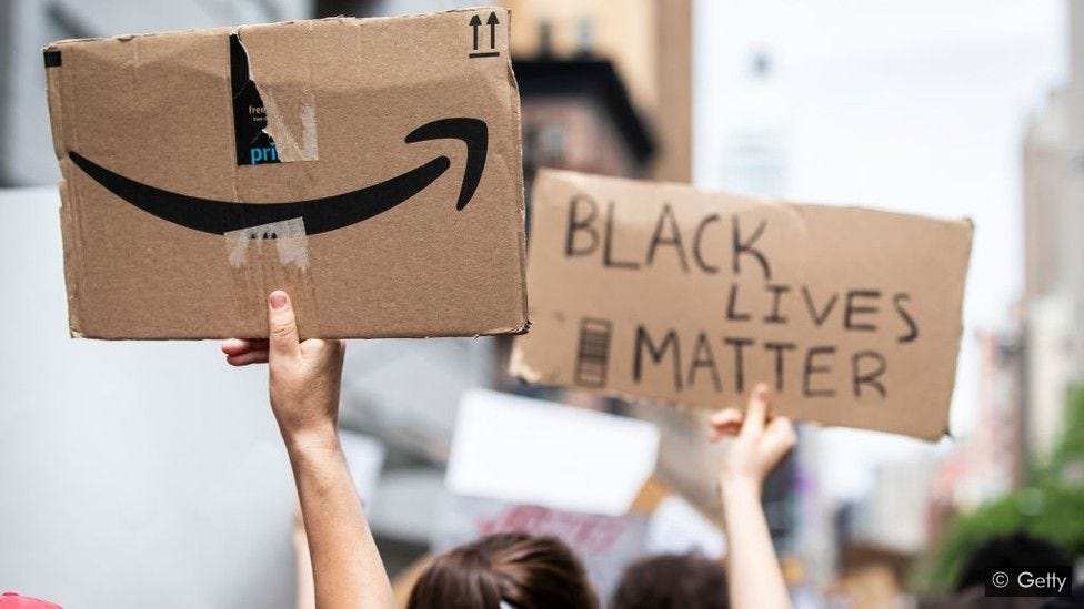 arms holding protest signs, one says Black Lives Matter, the other has an amazon logo