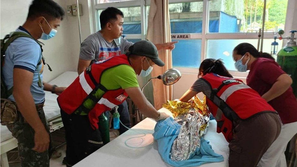 Philippine Red Cross workers workers putting a child wrapped in an emergency blanket on a hospital bed