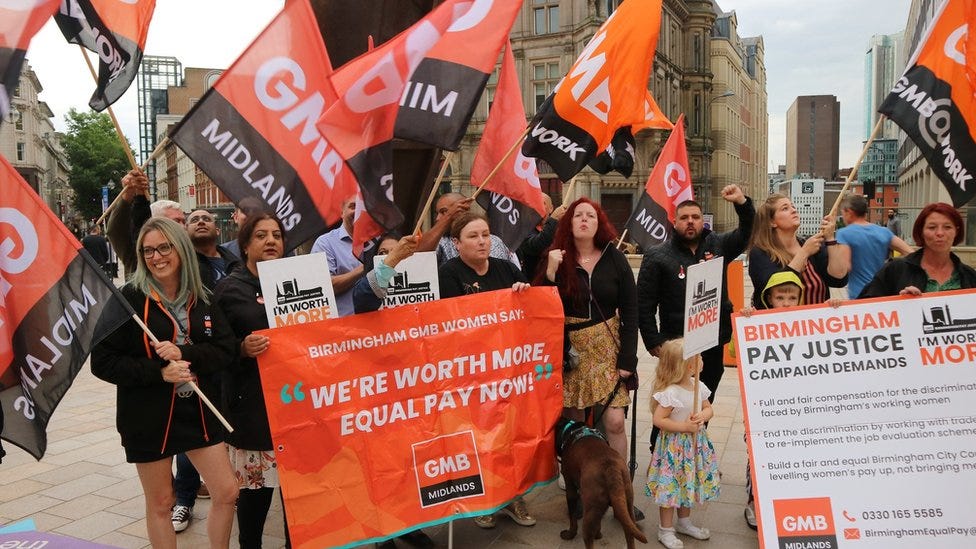 A group of protestors holding flags and a banner with the logo for GMB Midlands