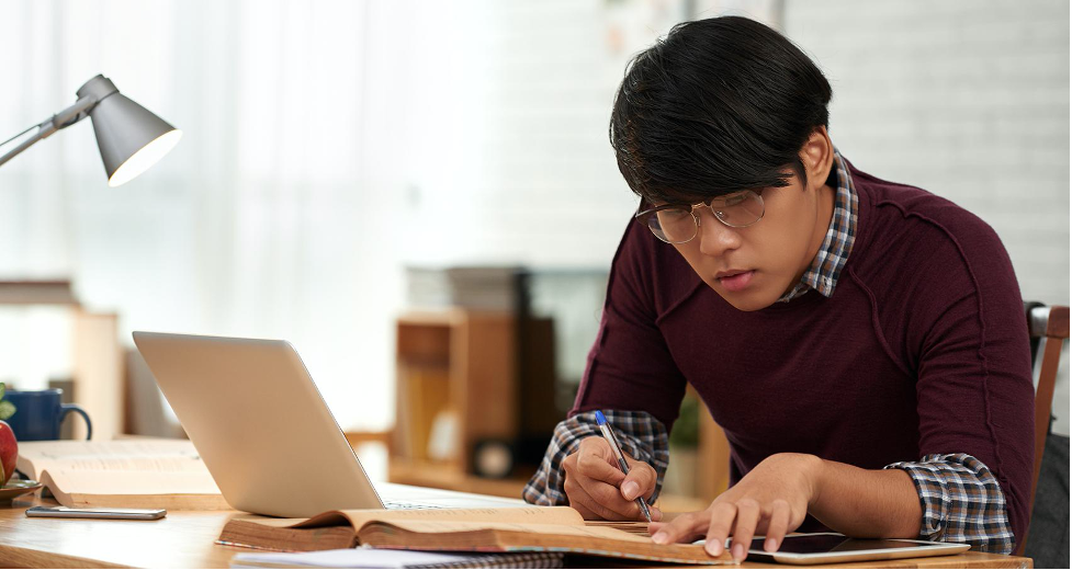 Young engineer wearing glasses and maroon sweater studying at computer