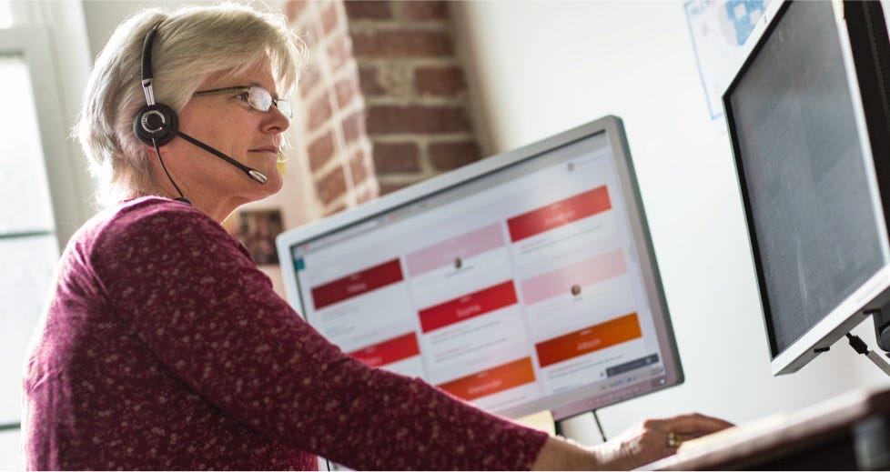 Nurse case manager with a telephone headset sitting at a computer monitor showing patient alerts