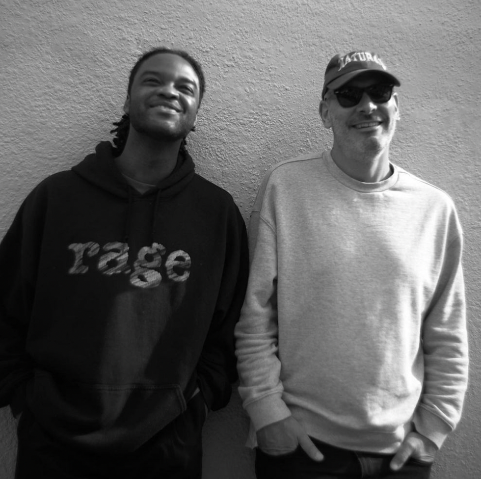 Genesis Owusu and Andrew Klippel both stand with their backs to a wall, smiling towards the camera in a relaxed moment. Genesis is wearing a RAGE hoodie. Andrew is wearing sunglasses and a cap.