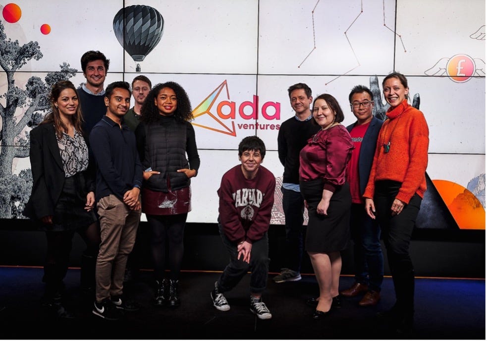 A group of 10 Ada Ventures Scouts standing in front of the Ada Ventures logo. The group is diverse and smiling at the camera.