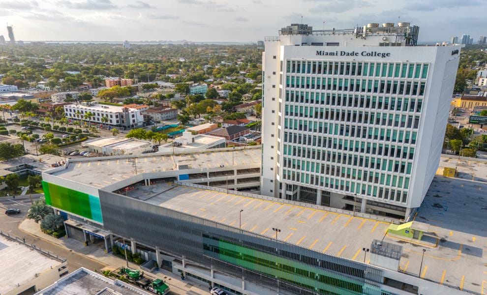 Aerial view of a large building featuring a vibrant green roof, surrounded by urban landscape and clear blue skies.