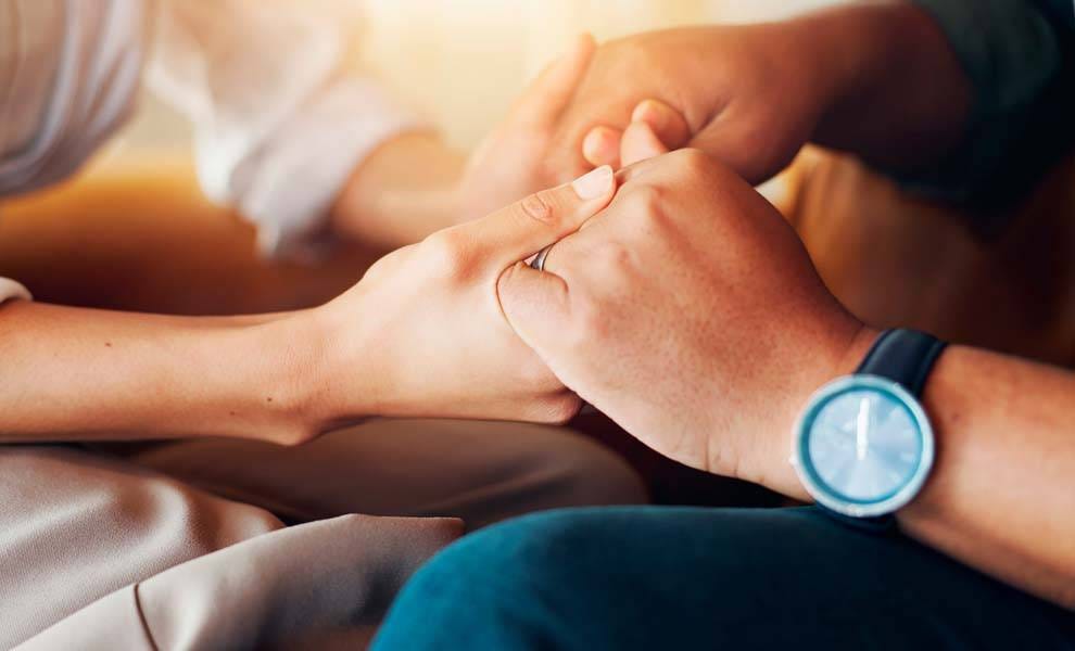 A man and woman sit together on a couch, holding hands and sharing a moment of connection and intimacy.