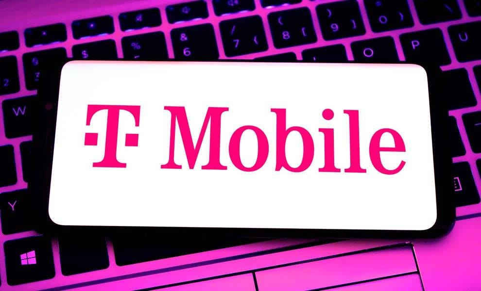 Logotipo de T-Mobile en la pantalla de un teléfono celular encima de un teclado de computadora.