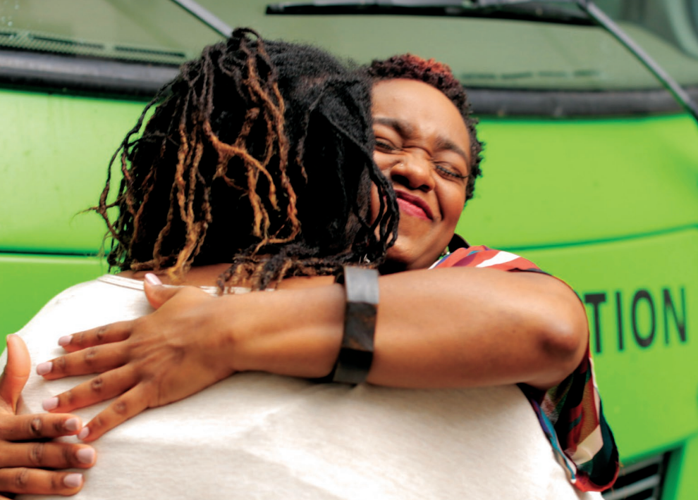 Two Black women hug in front of the Roadtrip Nation green RV.