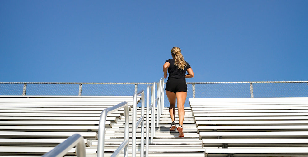 Christie running up stairs at a stadium towards a large blue sky.