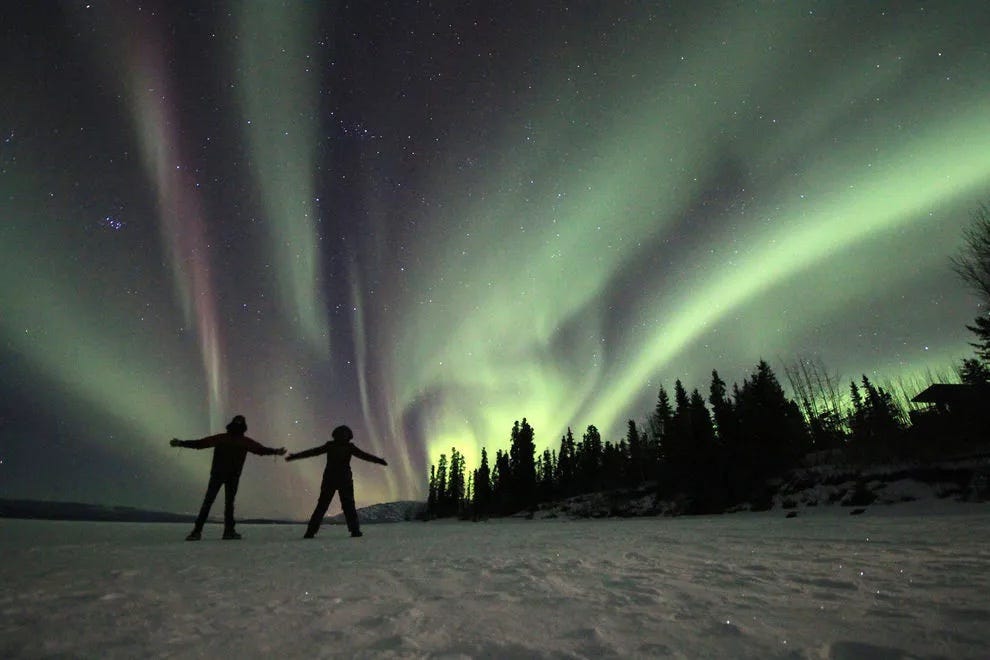Two lucky travelers take in the northern lights while standing on a frozen lake in th Yukon region of Canada.