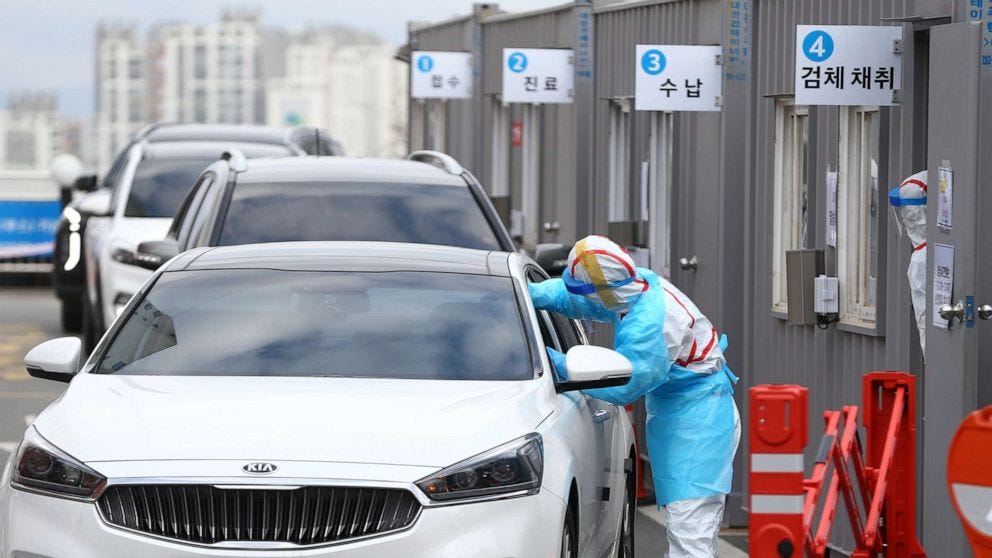 A person in full PPE reaches inside a car window to test the occupant for coronavirus