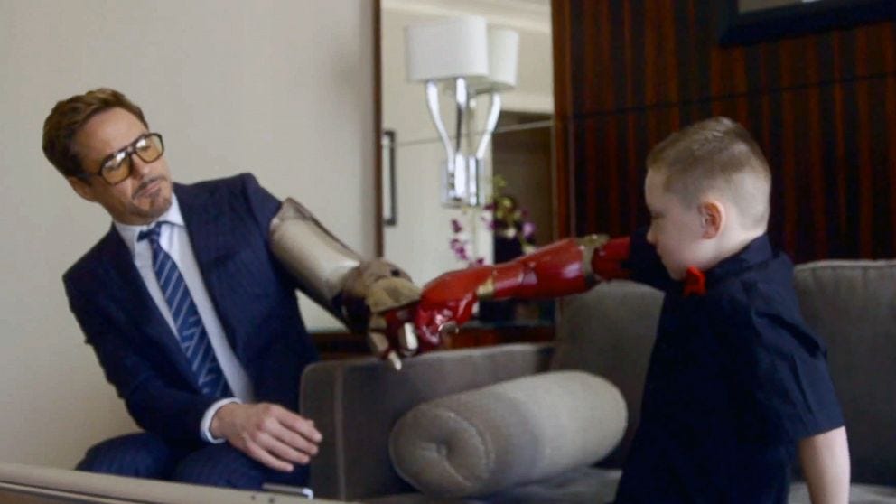 An image of Alex Pring, a 7-year-old boy with a newly-given Iron Man themed prosthetic arm, sharing a fist-bump with Robert Downey Jr., famously known for playing Tony Stark (Iron Man) in Marvel Movies.