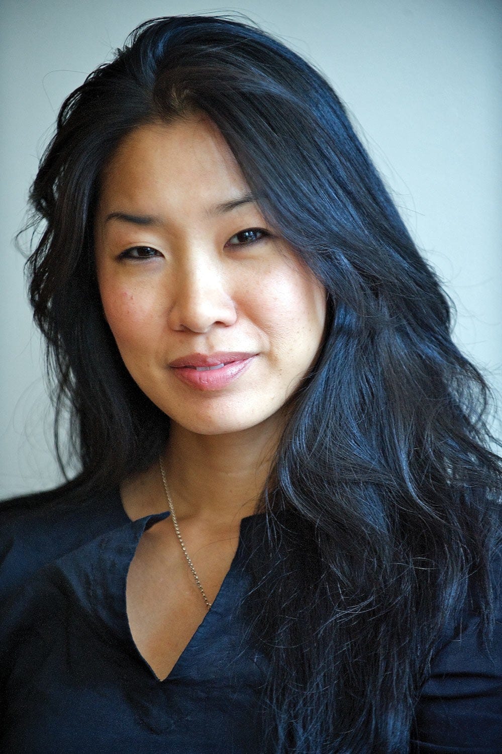 Chang in a black blouse, golden necklace strand across it.