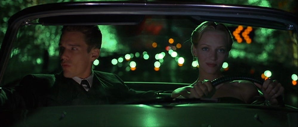 A still from Gattaca showing Vincent (Ethan Hawke) and Irene (Uma Thurman) seated in a vintage car at night, their expressions calm, the scene washed in green and orange city lights.