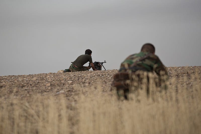 30/09/2015. Kirkuk, Iraq. Two peshmerga fighters hunker down as rounds from ISIS snipers and machine gunners fire at Kurds from the village of Mansuriya west of Kirkuk, Iraq. Supported by coalition airstrikes around 3500 peshmerga of the Patriotic Union of Kurdistan (PUK) and the Kurdistan Democratic Party (KDP) engaged in a large offensive to push Islamic State militants out of villages to the west of Kirkuk. During previous offensives ISIS fighters withdrew after sustained coalition air support, but this time in many places militants stayed and fought. The day would see the coalition conduct around 50 airstrikes helping the joint peshmerga force to advance to within a few kilometres of the ISIS stronghold of Hawija and re-take around 17 villages. Around 20 peshmerga lost their lives to improvised explosive devices left by the Islamic State, reports suggest that between 40 and 150 militants were killed.