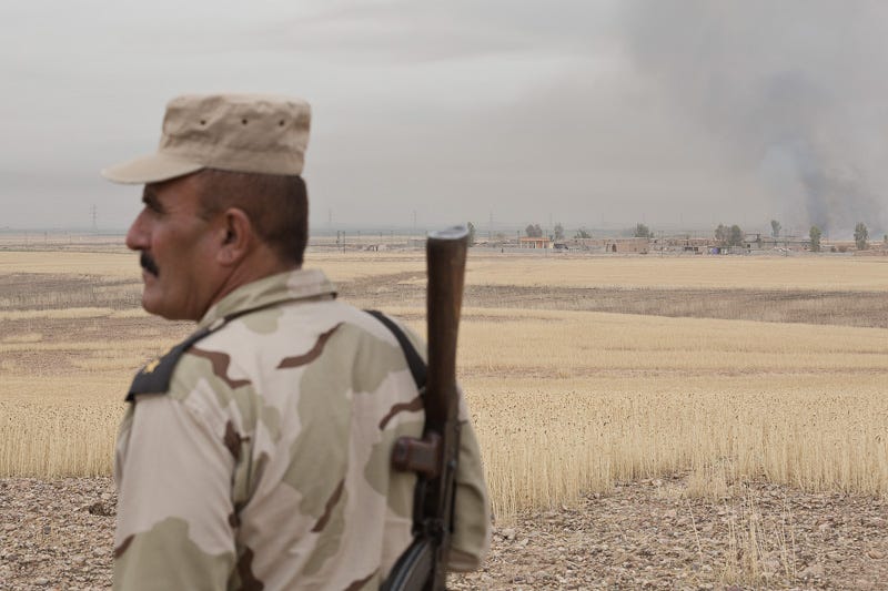 30/09/2015. Kirkuk, Iraq. A Kurdish KDP peshmerga lieutenant colonel stands on a hill as fields burn beyond the village of Mansuriya west of Kirkuk, Iraq. Supported by coalition airstrikes around 3500 peshmerga of the Patriotic Union of Kurdistan (PUK) and the Kurdistan Democratic Party (KDP) engaged in a large offensive to push Islamic State militants out of villages to the west of Kirkuk. During previous offensives ISIS fighters withdrew after sustained coalition air support, but this time in many places militants stayed and fought. The day would see the coalition conduct around 50 airstrikes helping the joint peshmerga force to advance to within a few kilometres of the ISIS stronghold of Hawija and re-take around 17 villages. Around 20 peshmerga lost their lives to improvised explosive devices left by the Islamic State, reports suggest that between 40 and 150 militants were killed.