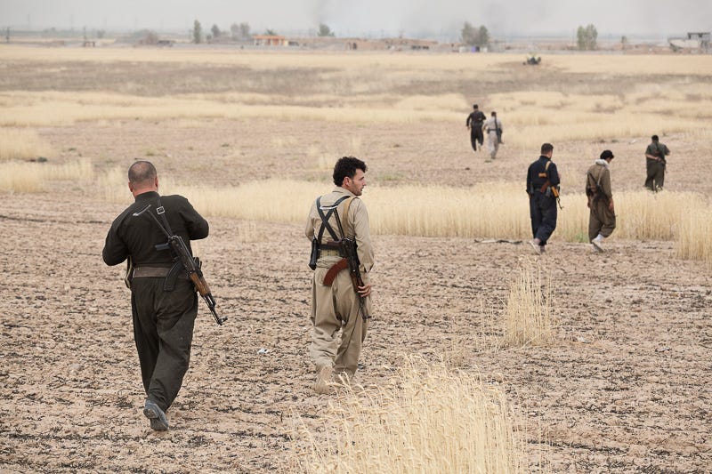 30/09/2015. Kirkuk, Iraq. Hadji Fazer (C) and his volunteer peshmerga advance towards a peshmerga armoured Humvee waiting on the edge of the formerly ISIS held village of Mansuriya, west of Kirkuk, Iraq. Supported by coalition airstrikes around 3500 peshmerga of the Patriotic Union of Kurdistan (PUK) and the Kurdistan Democratic Party (KDP) engaged in a large offensive to push Islamic State militants out of villages to the west of Kirkuk. During previous offensives ISIS fighters withdrew after sustained coalition air support, but this time in many places militants stayed and fought. The day would see the coalition conduct around 50 airstrikes helping the joint peshmerga force to advance to within a few kilometres of the ISIS stronghold of Hawija and re-take around 17 villages. Around 20 peshmerga lost their lives to improvised explosive devices left by the Islamic State, reports suggest that between 40 and 150 militants were killed.