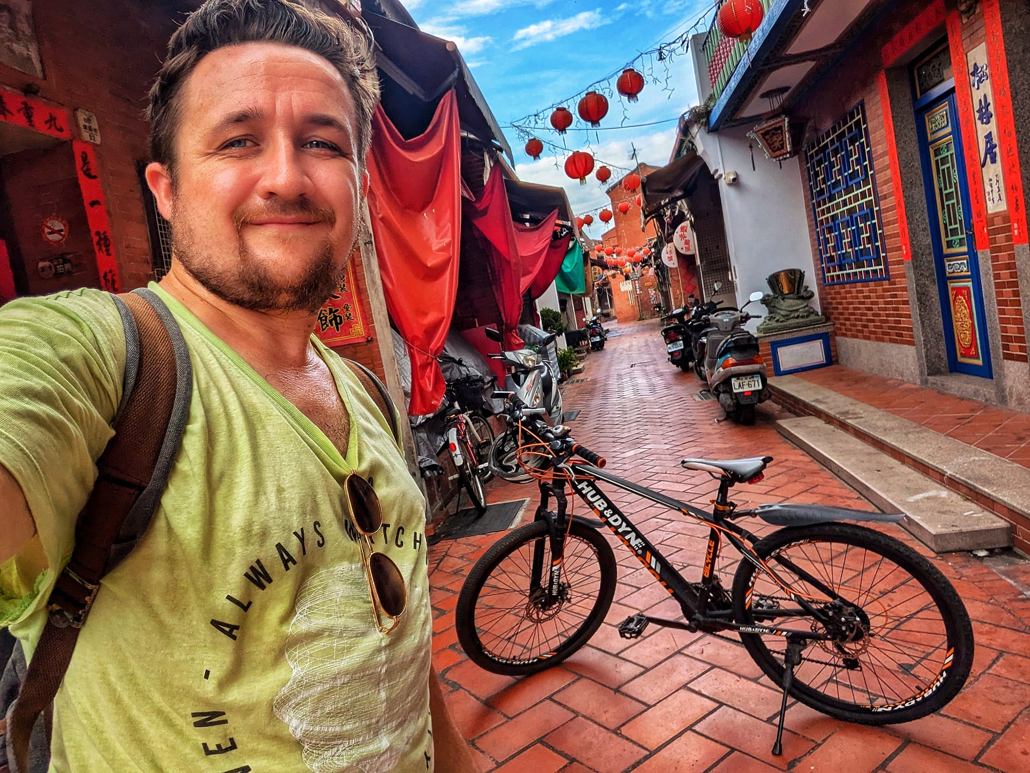 The author wearing a yellow shirt takes a selfie with his bike in the background on an alley.