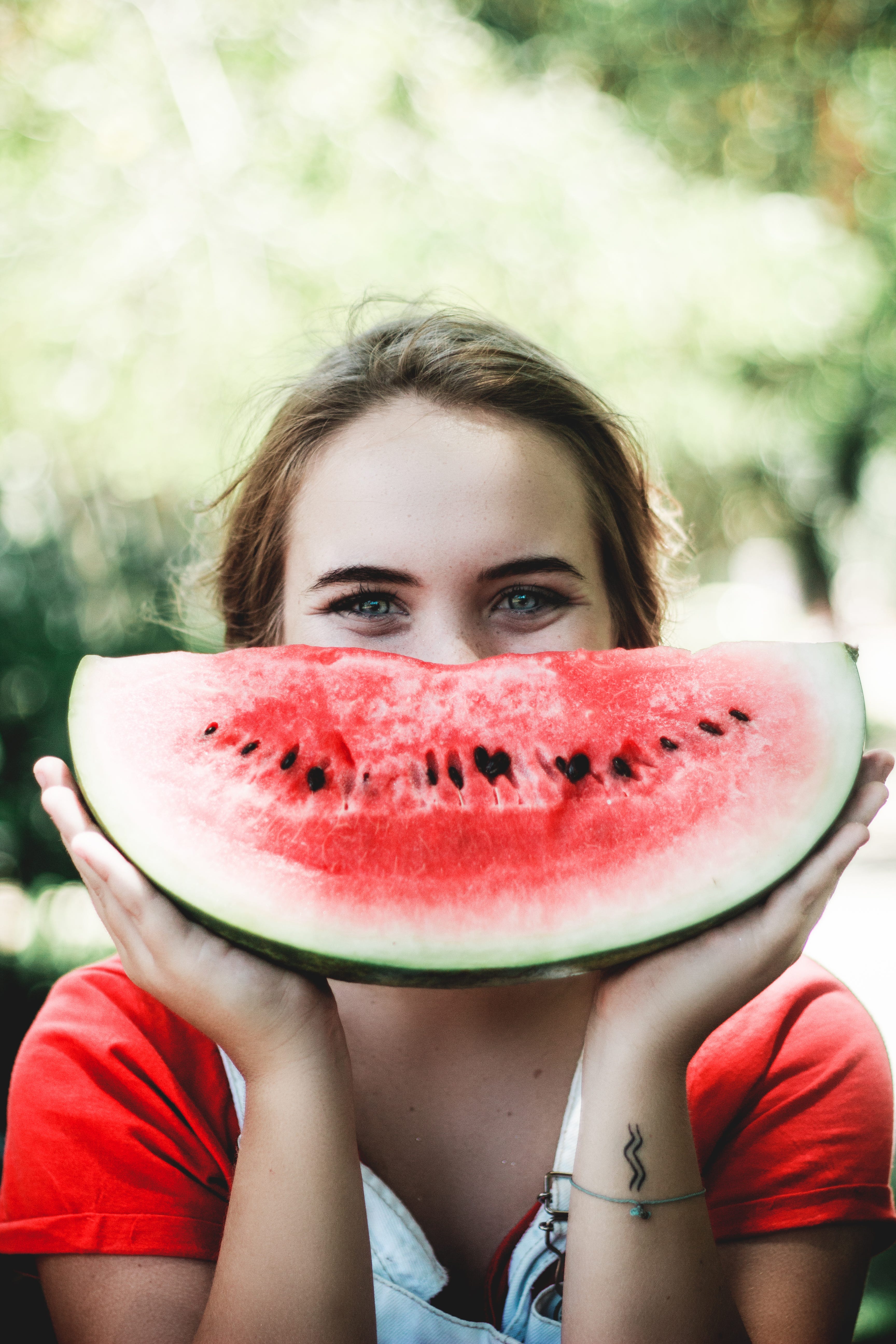 Picture of a smiling woman holding a large slice of watermelon in front of her face