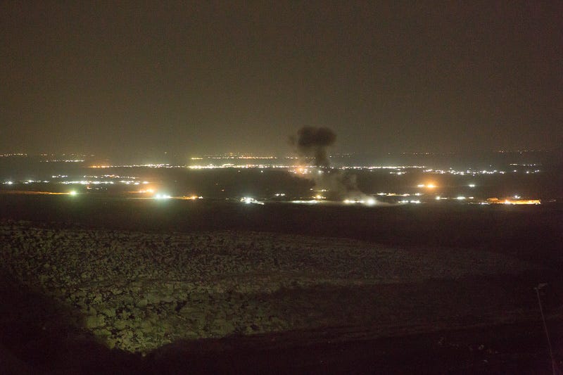 01/09/2015. Bashiqa, Iraq. A puff of smoke marks the spot where a coalition aircraft dropped a bomb on ISIS vehicles moving through the town of Bashiqa, Iraq. The ISIS heald city of Mosul can be seen illuminated in the background. Bashiqa Mountain, towering over the town of the same name, is now a heavily fortified front line. Kurdish peshmerga, having withdrawn to the mountain after the August 2014 ISIS offensive, now watch over Islamic State held territory from their sandbagged high-ground positions. Regular exchanges of fire take place between the Kurds and the Islamic militants with the occupied Iraqi city of Mosul forming the backdrop. The town of Bashiqa, a formerly mixed town that had a population of Yazidi, Kurd, Arab and Shabak, now lies empty apart from insurgents. Along with several other urban sprawls the town forms one of the gateways to Iraq's second largest city that will need to be dealt with should the Kurds be called to advance on Mosul.