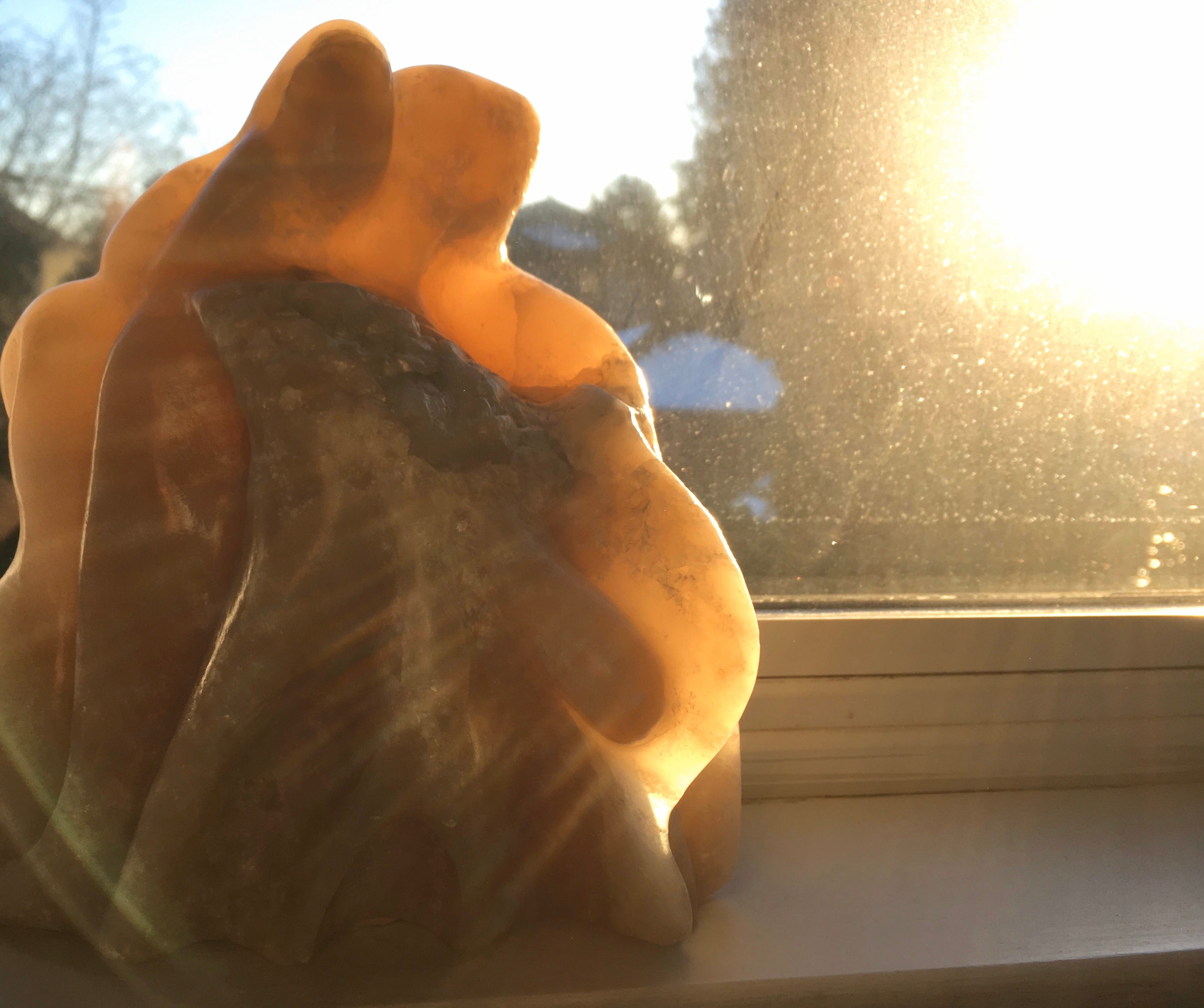 Winter sun shines around and through warm beige alabaster carved with 2 figures looking down together holding a child