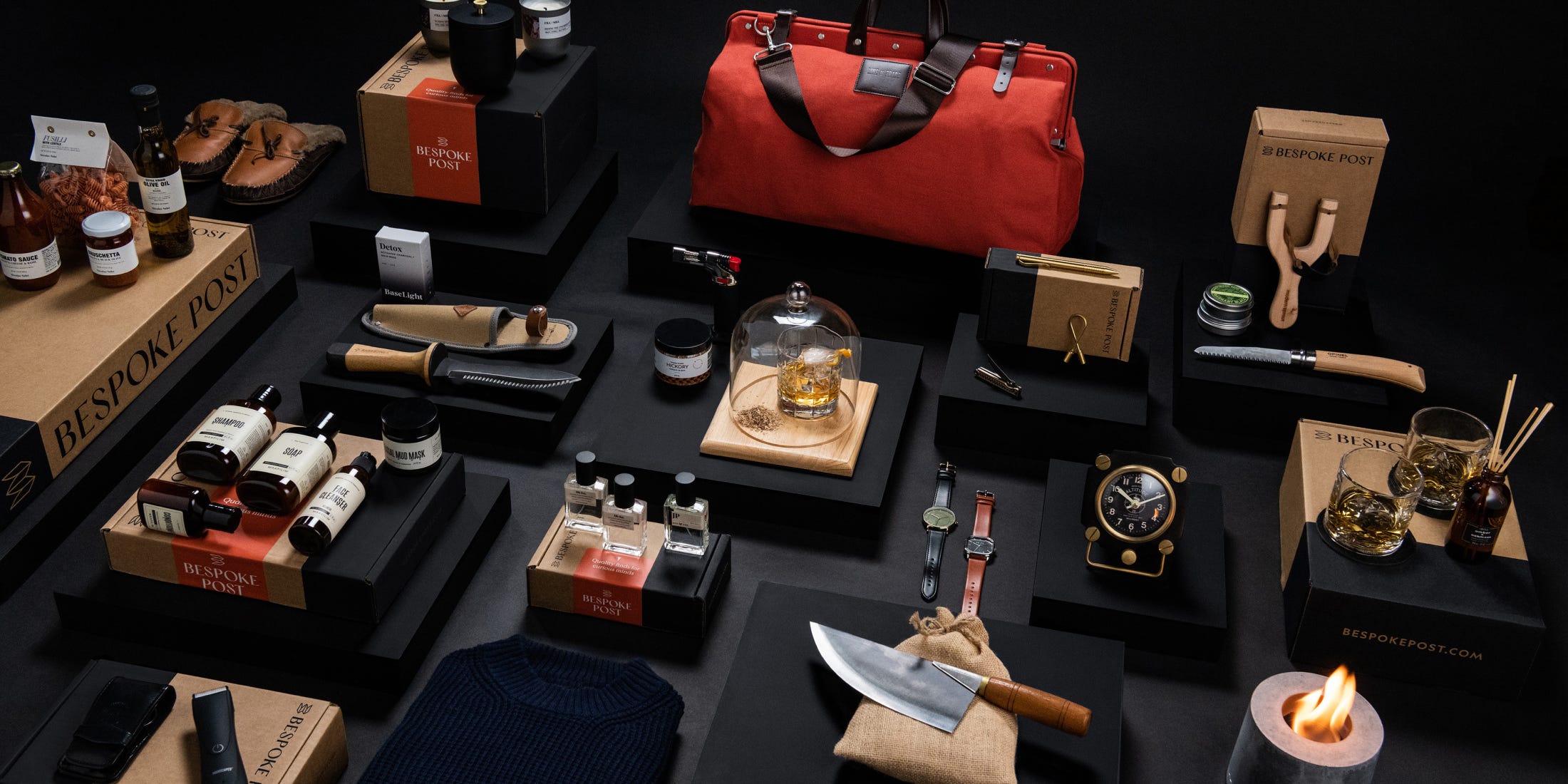 A layout of things on boxes: different size bottles of shampoo, soap, face cleanser, a jar of mud mask, a clock, a chef’s knife, a red duffel bag, slippers, a slingshot, a bottle of incense, two wrist watches, an electric shaver, three candles, a woolen sweater, a flame torch, a nail clipper, a copper pen, a bag of fusilli, tomato sauce, and olive oil.