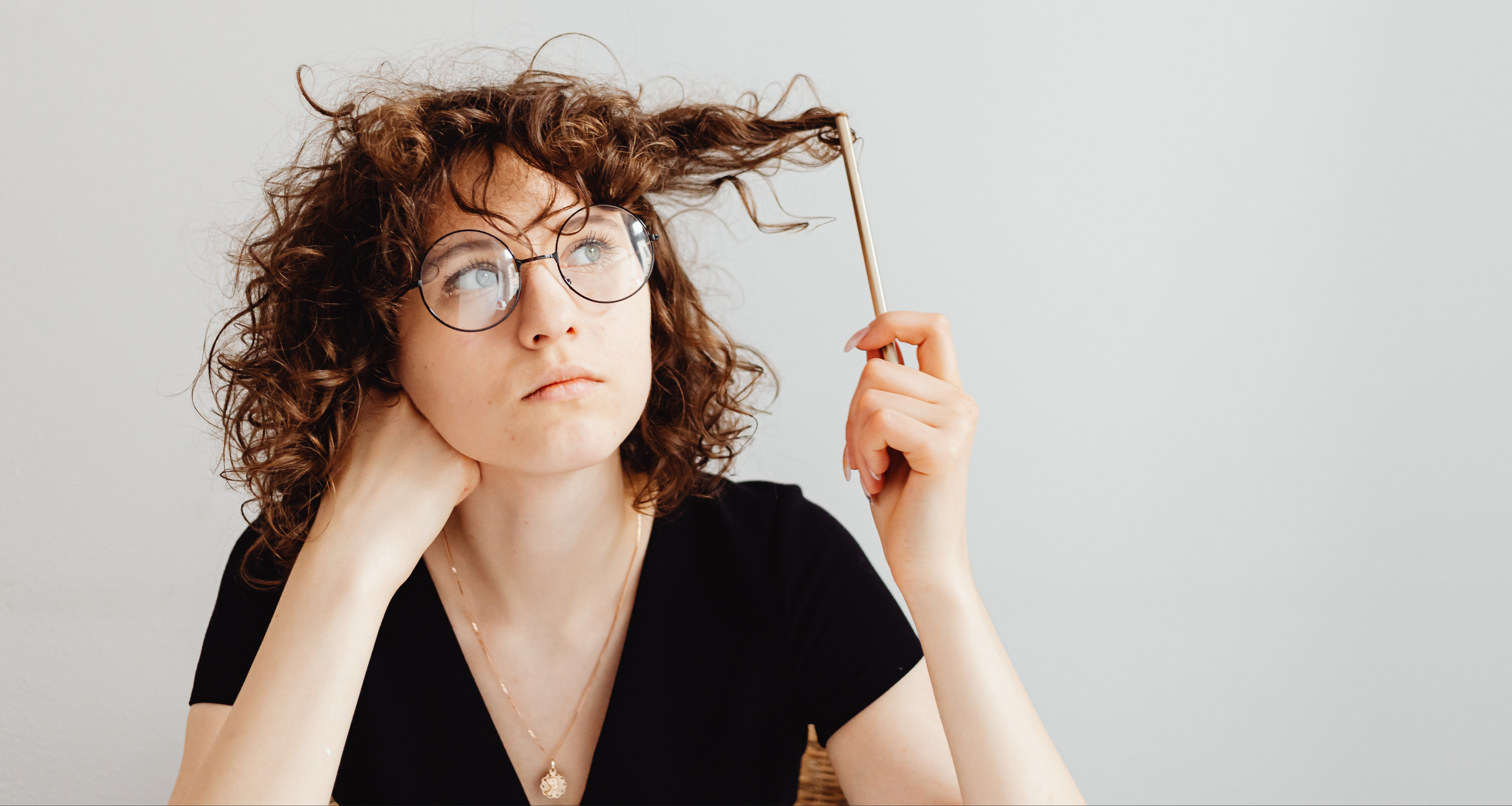 A brown-headed woman in a V-neck shirt is playing with her hair. Karolina Grabowska/Canva.