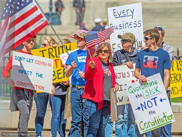 A group of protestors hold American flags and posters against Covid-19 quarantine protocols.