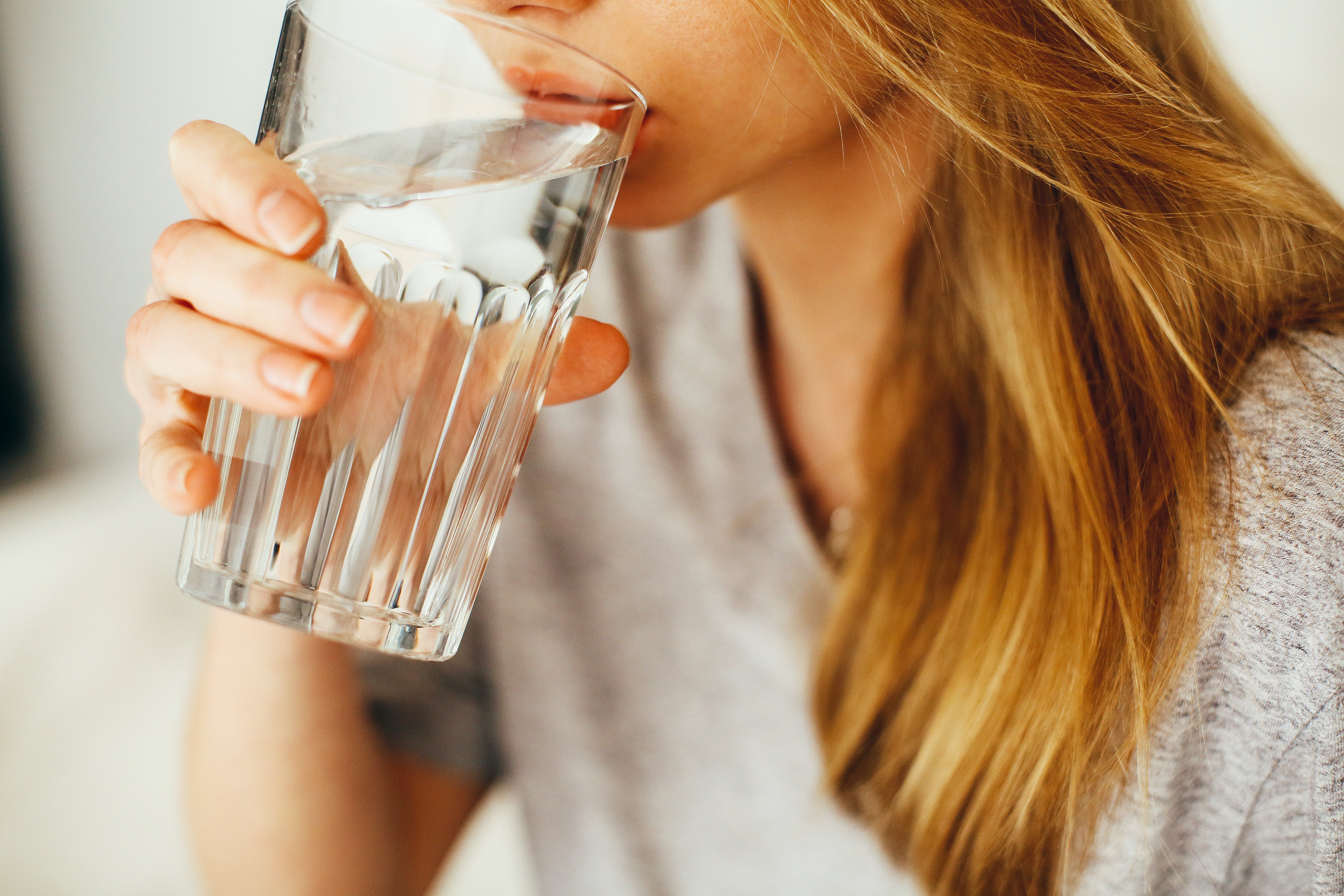 A blonde woman takes a sip out of a water glass